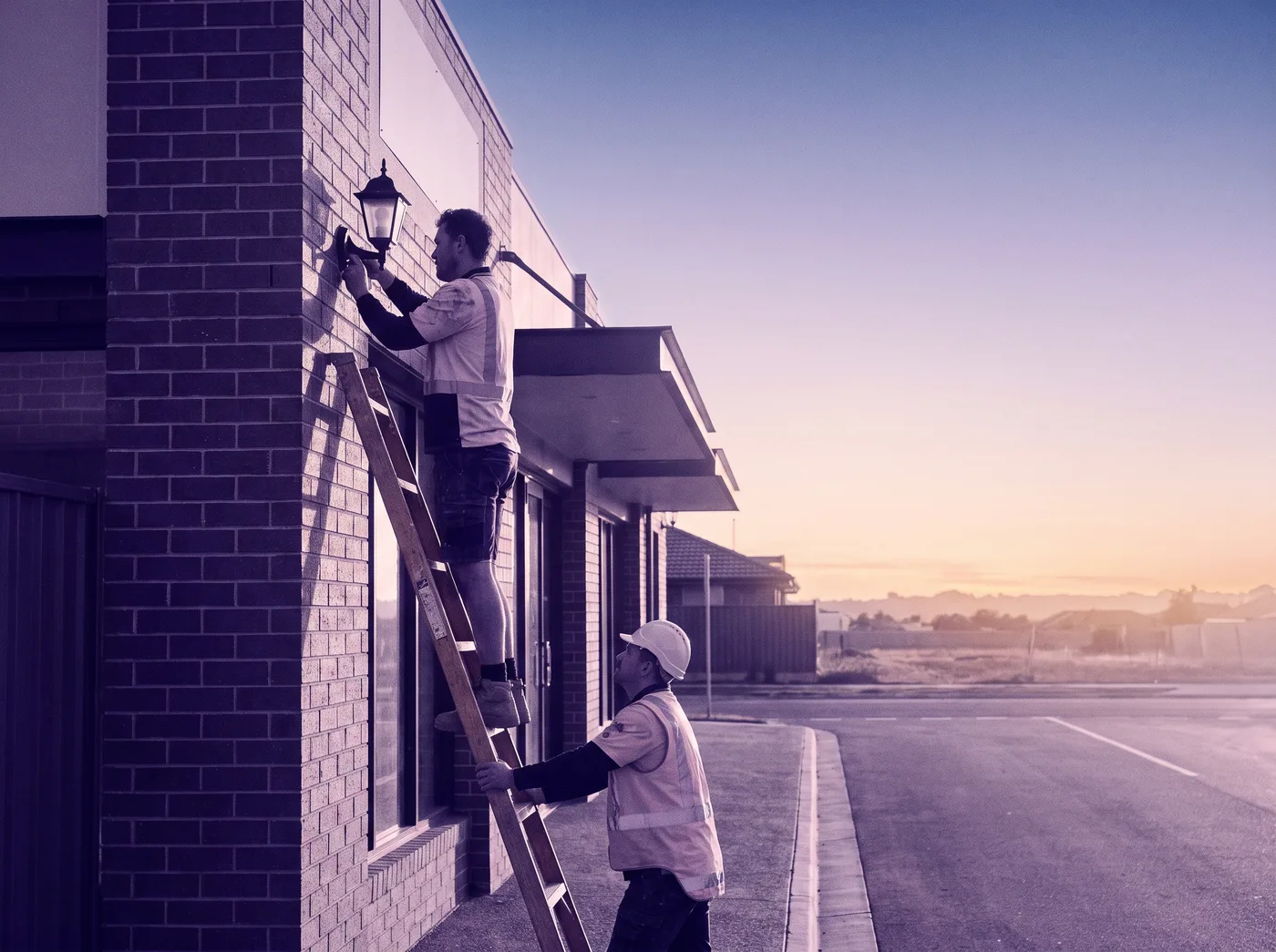 Two tradespeople installing a light on a shopfront at dawn