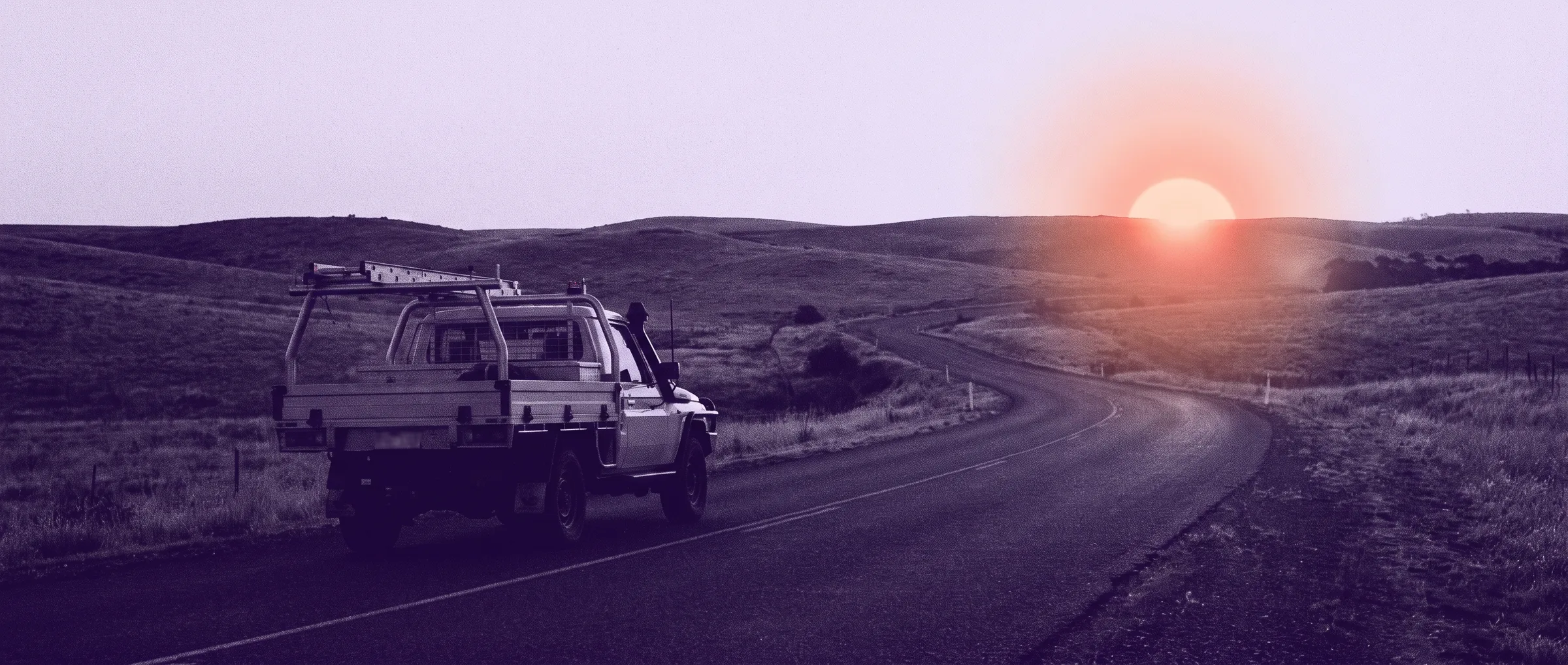 A tradie's ute on an open country road at dawn, sun cresting the hills